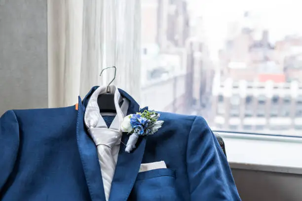 Men's suit and tie groom closeup with flower boutonniere, pin wedding preparation, pocket handkerchief, window with view of urban New York City NYC Manhattan cityscape, skyline