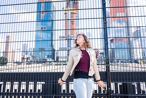 Young hipster millennial woman looking at Hudson Yards in NYC New York City Manhattan downtown on high line park and trains behind fence, tourist looking up