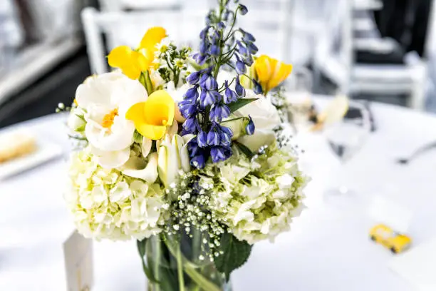 Closeup of one wedding flower bouquet arrangement on table of reception dinner in restaurant venue, black bokeh background, chairs