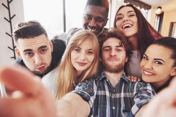 istock Friends having fun at restaurant.Two boys and four girls drinking making selfie, making peace sign and laughing. On foreground woman holding smart phone. All wear casual clothes 961960156