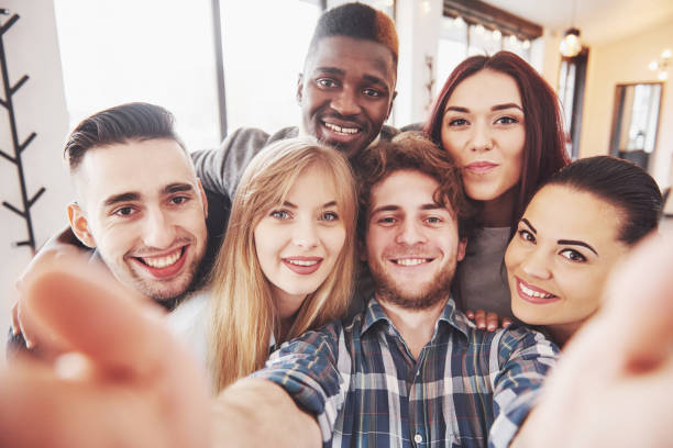 istock Friends having fun at restaurant.Two boys and four girls drinking making selfie, making peace sign and laughing. On foreground woman holding smart phone. All wear casual clothes 961960196