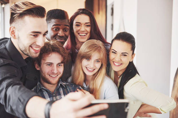 istock Friends having fun at restaurant.Two boys and four girls drinking making selfie, making peace sign and laughing. On foreground woman holding smart phone. All wear casual clothes 961960246