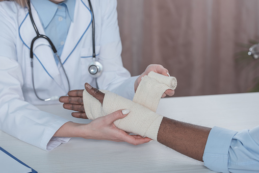 Cropped image of doctor bandaging african american patient hand