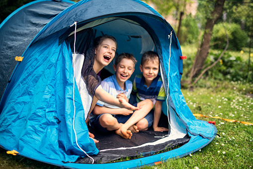 Kids aged 8 and 12 are laughing happily sitting inside of blue tent - playing camping in garden. Kids are surprised by summer rain.
Nikon D850