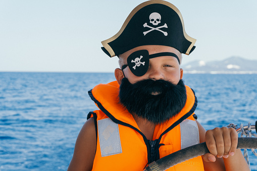 Boy wears pirate costume with eye patch and hat and steering sailboat