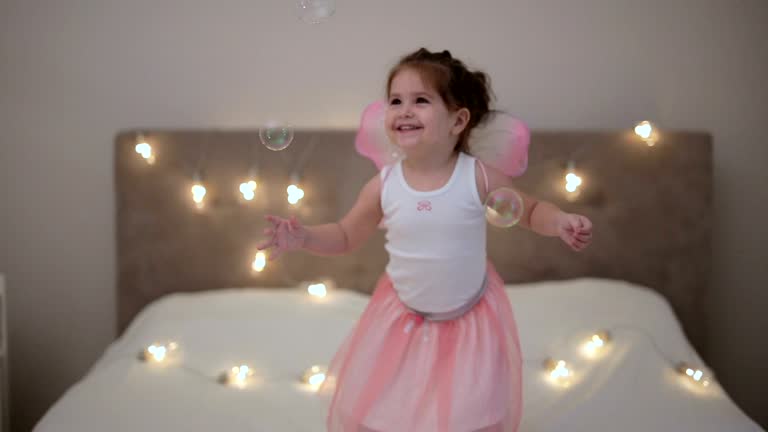 Toddler with fairy wings playing in the bedroom.