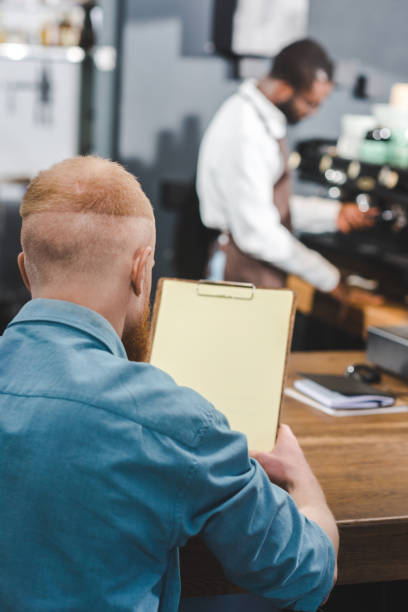 istock back view of man holding blank clipboard while barista making coffee behind 961982232