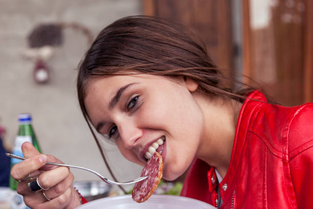 portrait of cute girl while eating a slice of salami stock photo