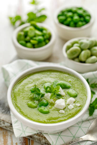 sopa de favas com queijo fresco de hortelã e queijo feta em uma tigela branca em uma mesa de madeira. - pea and mint soup - fotografias e filmes do acervo