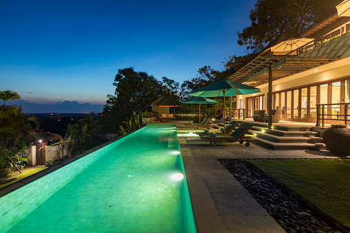 Located near Uluwatu in Bali, a luxurious villa with a swimming pool is illuminated during an early sunrise. The real estate property faces south with a stunning view on the Indian ocean