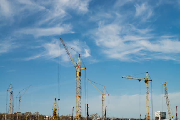 istock Big tower cranes above buildings under construction against blue sky. Background image of construction close-up with copy space. Build of city. 962000584