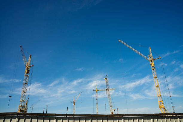 istock Big tower cranes above buildings under construction against blue sky. Background image of construction close-up with copy space. Build of city. 962000646