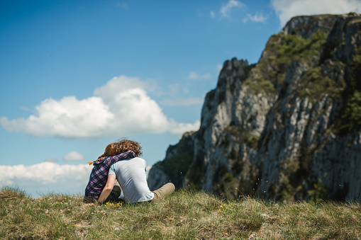 Young couple hiking in mountain and relaxing looking at view, lying down in the grass, enjoying together