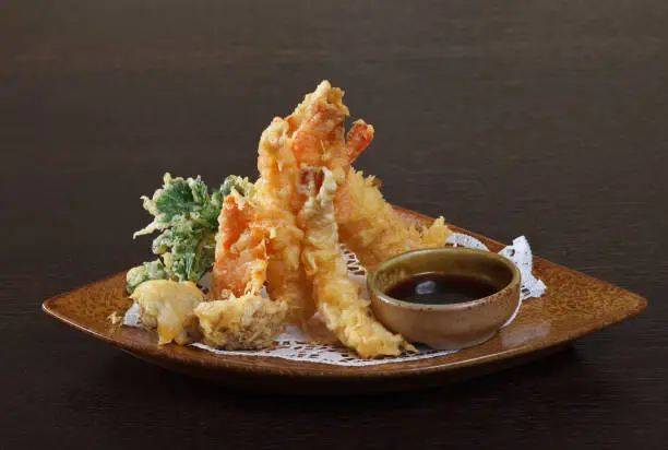 Tempura shrimps (deep fried shrimps) with soy sauce on wooden background.