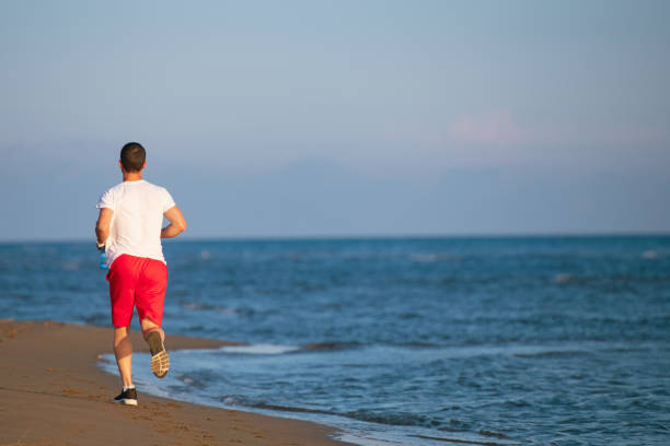 istock Man running on the beach at sunset 962028282