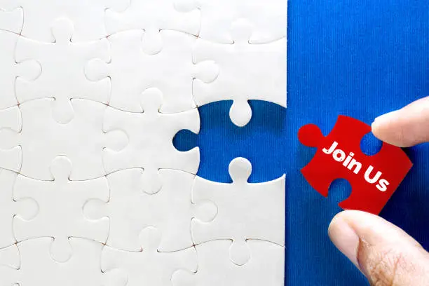 Photo of Close up piece of white jigsaw puzzle with Join Us text , concept of a business challenge success completion with teamwork