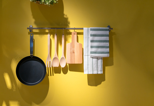 Kitchen utensils and towel hanging on metal rack against yellow background.