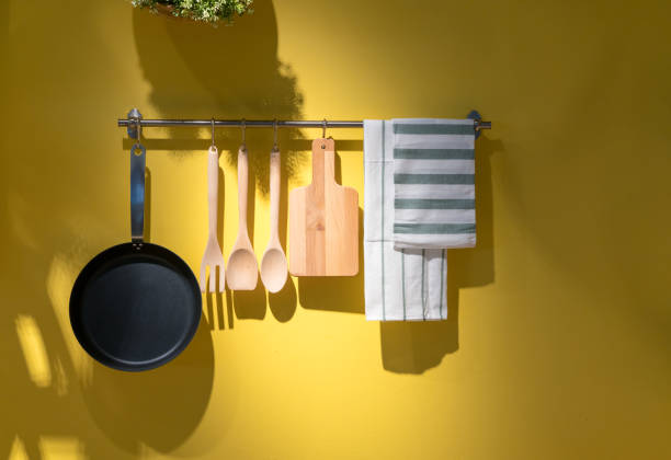 Kitchen utensils and towel hanging on metal rack against yellow background. stock photo