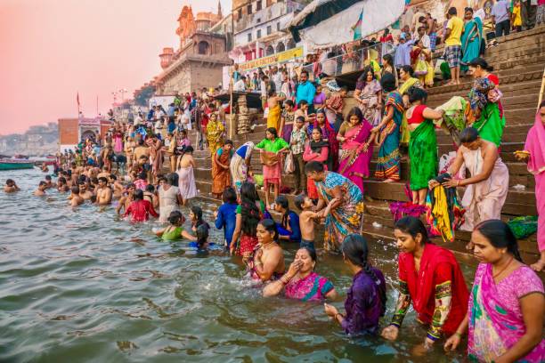 Close-up view of a large group of Hindu pilgrims wearing colorful clothing and traditional saris are gathered on the ghats of Varanasi to bathe in the holy water of the Ganges River. stock photo