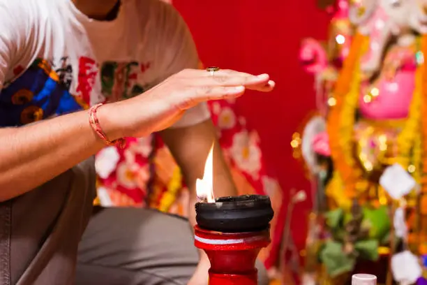 a hand taking heat of the flame as blessing from a lit clay lamp on top of a clay stand or worship idol durgapuja india diwali