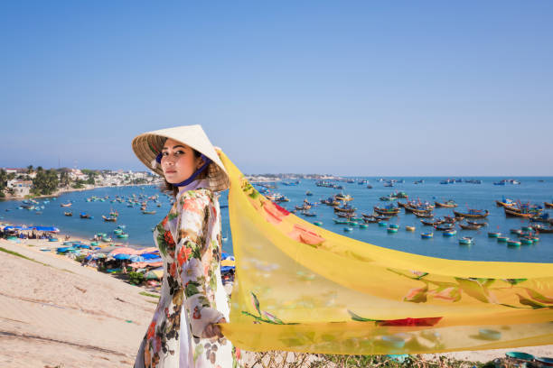 Woman wearing Ao Dai culture traditional wait at the harbor. Vietnam woman wearing Ao Dai culture traditional and conical hat wait at the harbor at Mui Ne in Vietnam,vintage style,travel and relaxing concept. mui ne bay photos stock pictures, royalty-free photos & images
