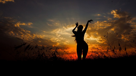 Female person doing yoga in steppe, silhouette in sunset background. Concept of dancing meditation and relaxing on nature.