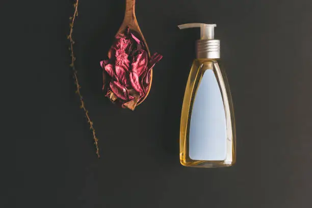 Moisturizing body and hair oil, with rose-petals. Lie on a black table, top view. Dark moody background