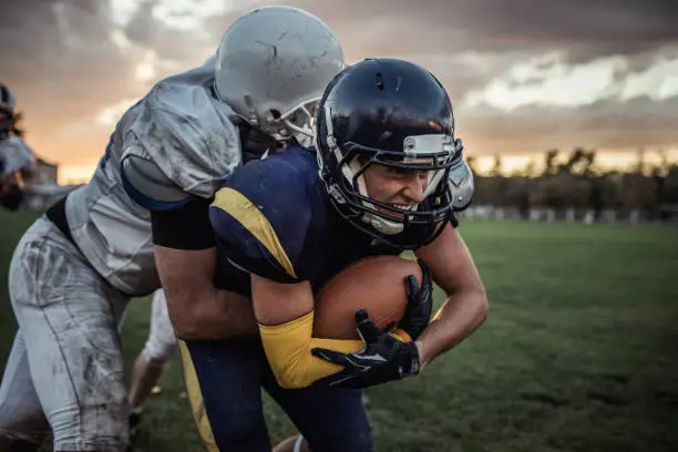 Young American football player making an effort while passing through defensive players with a ball.