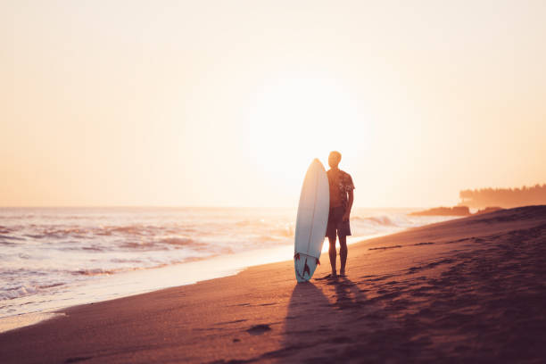 istock Silhouette of surfer with a surfboard on the beach at sunset 962077398