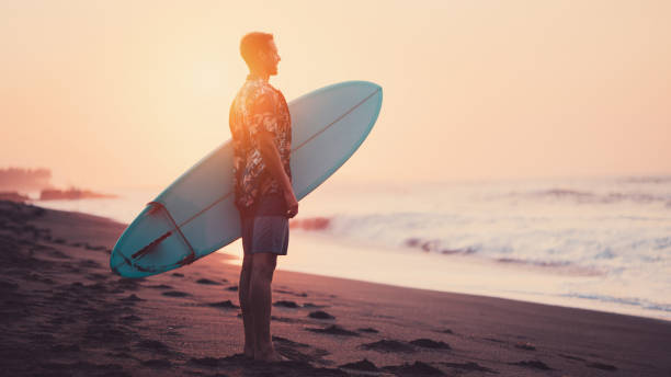 istock Silhouette of surfer with a surfboard on the beach at sunset 962077700