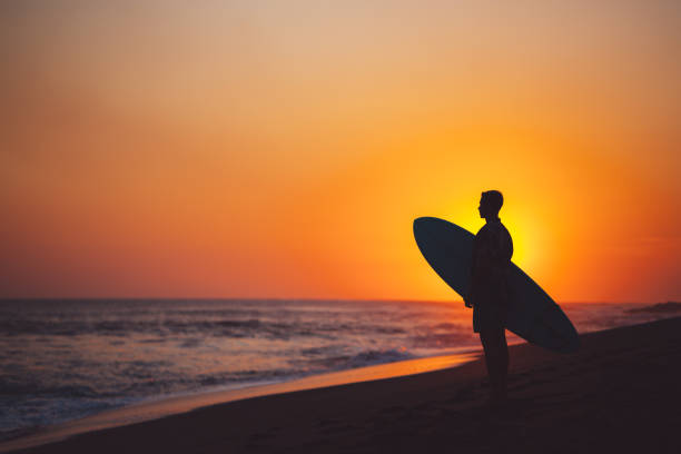 silhueta de surfista com uma prancha de surf na praia ao pôr do sol - wave salt surf sea - fotografias e filmes do acervo