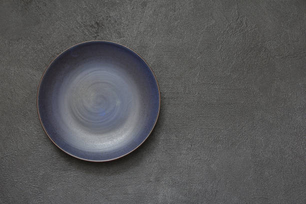 istock Blue round porcelain empty plate on a black stone background. Empty plate top view. 962077972