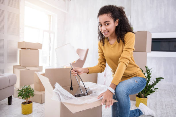 istock Upbeat curly girl putting lamp into box while packing 962088742