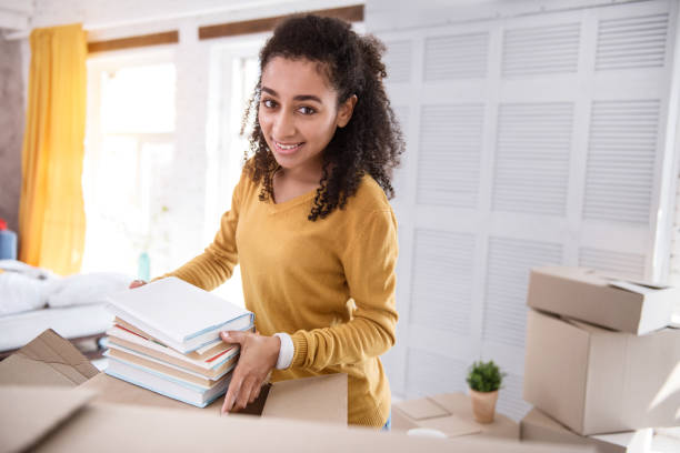 istock Pleasant curly-haired girl posing while packing books 962089128