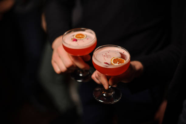 deux personnes tenant des verres à cocktail avec une boisson alcoolisée sucrée - cocktail alcohol red martini glass photos et images de collection