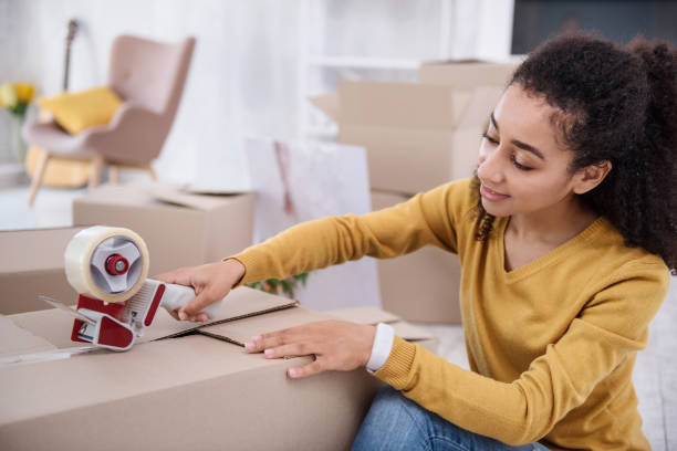 istock Pleasant curly-haired girl sealing box with adhesive tape 962089816