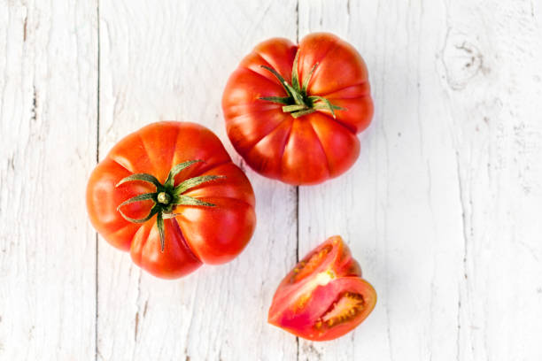 große rote frische tomaten ganze und halbierte auf alten holztisch im rustikalen stil, ansicht von oben - beefsteak tomato stock-fotos und bilder