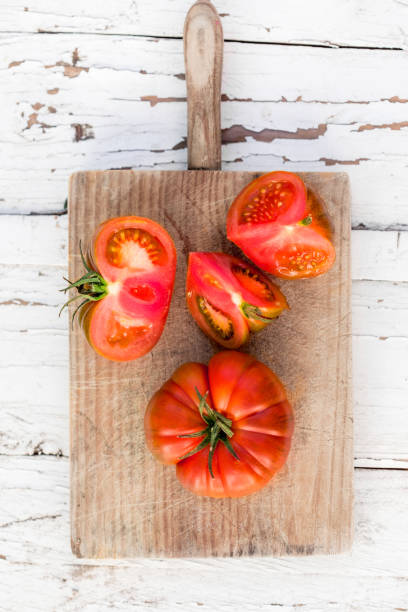 Raw delicious tomatoes  on cutting board on  old wooden table in rustic style, top view. Beefsteak tomatoes type