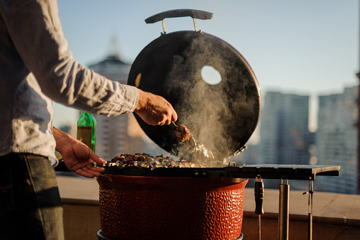 Man cooking a dish in a barbecue grill equipped with cooking tools standing on the roof of a building