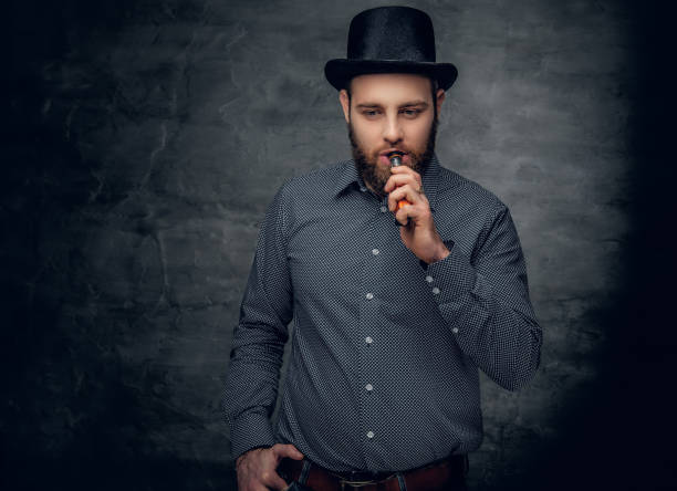 istock Bearded male smoking electronic cigarette over grey background. 962123110