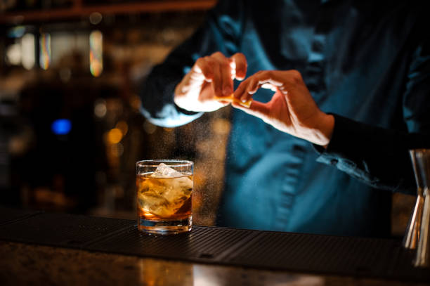 istock Bartender sprinkling orange peel juice into a cocktail glass 962125592
