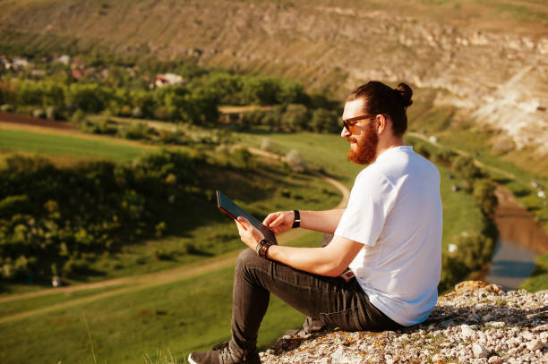 istock Happy bearded man sitting outside in nature and using tablet at sunset 962134628
