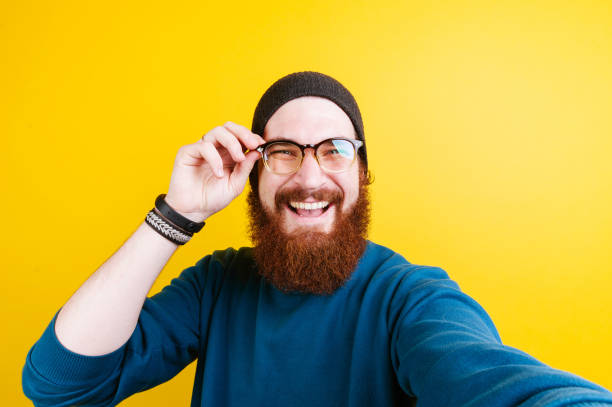 istock Smiling bearded hipster man touching eyeglasses and looking confident at the camera 962135112