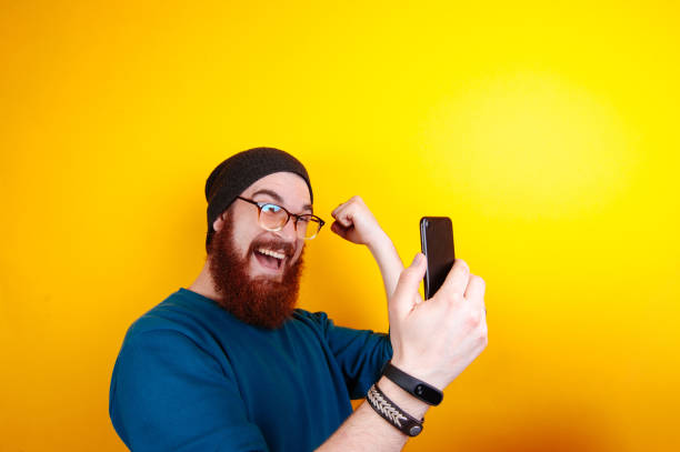 istock Happy excited young bearded hipster man using cell phone and celebrating success over yellow background 962135174