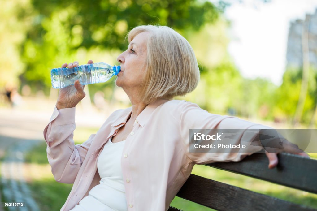 Adult woman in park Adult woman is sitting in park and drinking water. Senior Adult Stock Photo