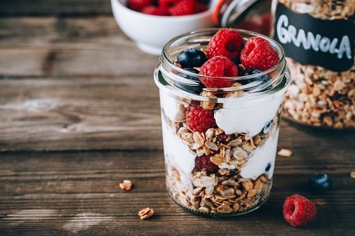 Healthy blueberry and raspberry parfait with greek yogurt in glass mason jar on rustic wood background