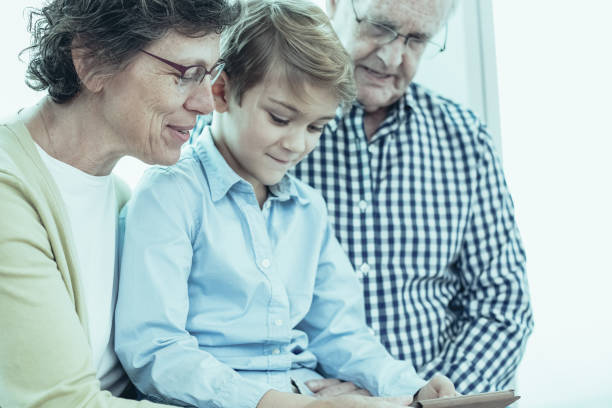 istock Modern boy with grandparents using tablet. They watching educational movie together and enjoying easy way to receive knowledge. Family spending time together. Modern education concept 962146956