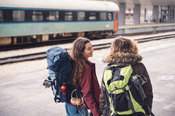 istock Female couple holding hands and talking while standing on the train station platform 962150262