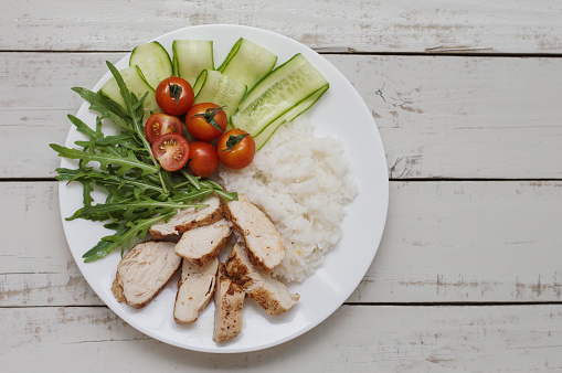 Healthy meal: baked chicken breast, white cooked rice, red cherry tomatoes, slices cucumber and fresh arugula leaves