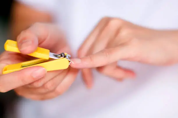 A woman is cutting fingernail of pinky in close-up and soft focus.